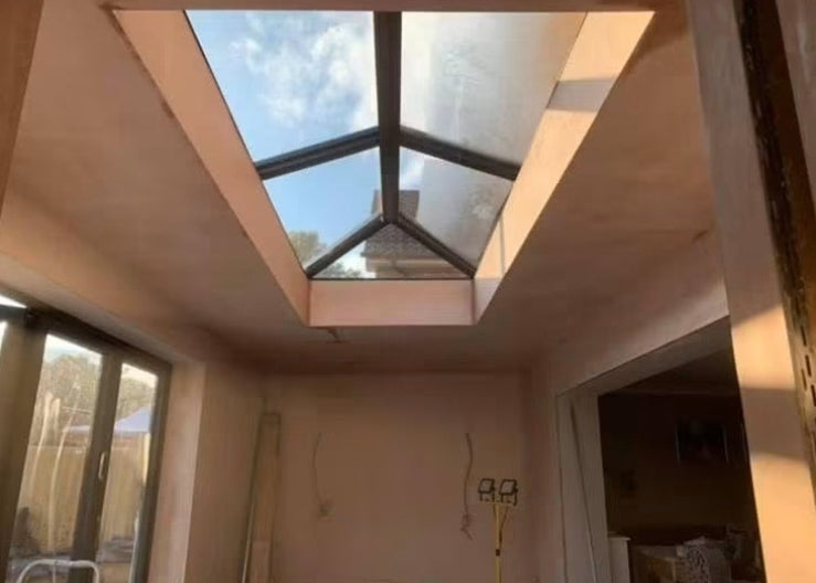 A tall interior room view looking up at a skylight with a glass panel and dark metal frame, with beige walls and daylight visible through the opening.