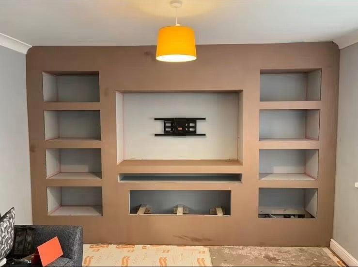 A built-in wall entertainment center with open shelving on both sides, a central media console, and a recessed wall niche, shown in a home interior setting with a yellow pendant light above.