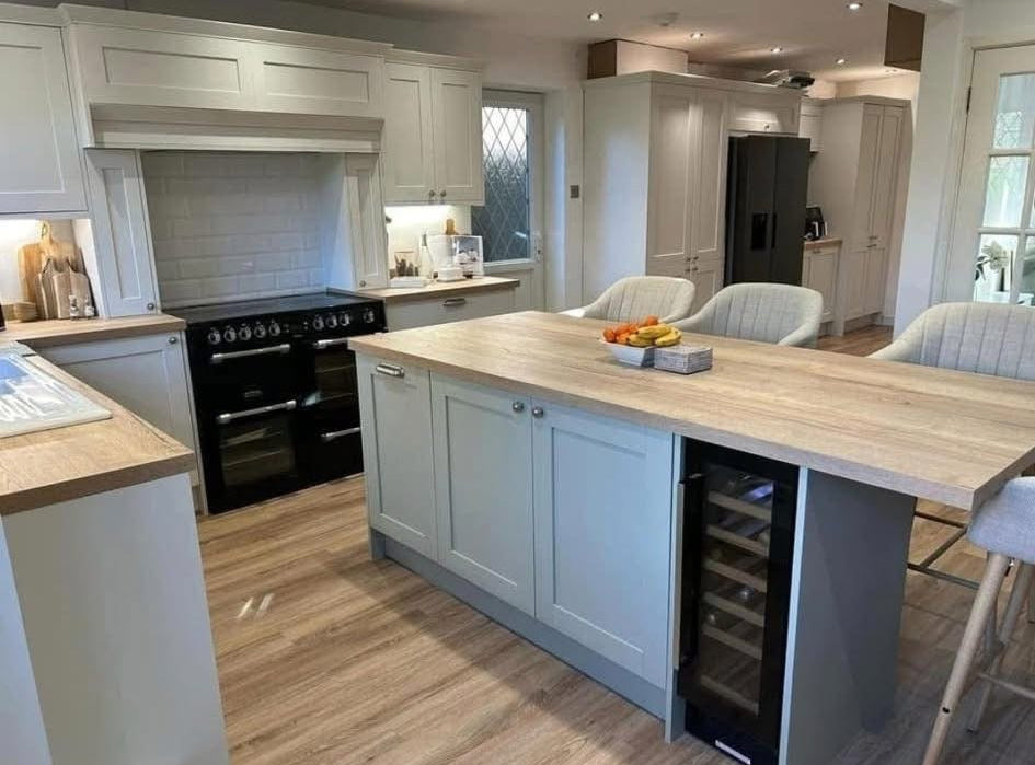 A modern kitchen island with a light wood countertop and white cabinetry, featuring a built-in wine cooler, set in a spacious kitchen with wood floors and black appliances.